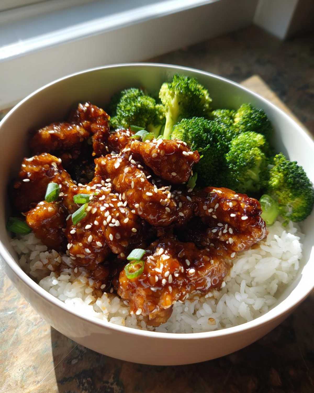 A close-up of a Honey Soy Chicken Bowl Quick Dinner Idea featuring glazed chicken pieces over white rice with steamed broccoli.