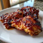 Close-up of three glistening Honey Soy Chicken Thighs with crispy, caramelized edges served on a white plate.