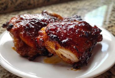 Close-up of two glistening Honey Soy Chicken Thighs with crispy, caramelized edges on a white plate.