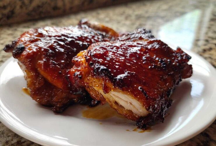 Close-up of two glistening Honey Soy Chicken Thighs with crispy, caramelized edges on a white plate.
