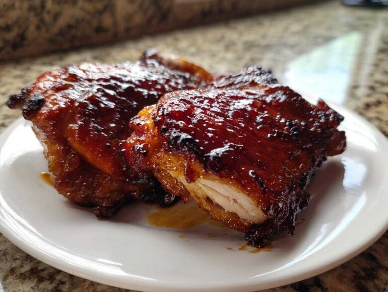 Close-up of two glistening Honey Soy Chicken Thighs with crispy, caramelized edges on a white plate.