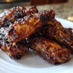 Close-up of several sticky and crispy Honey Sriracha Chicken Wings piled on a white plate.