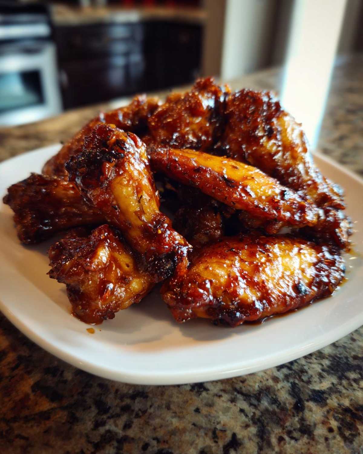 Close-up of a pile of sticky and crispy Honey Sriracha Chicken Wings coated in a dark, glossy sauce on a white plate.