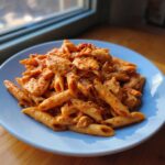 A plate piled high with One Pot Creamy Tomato Pasta with Chicken, featuring penne pasta and chunks of seasoned chicken.