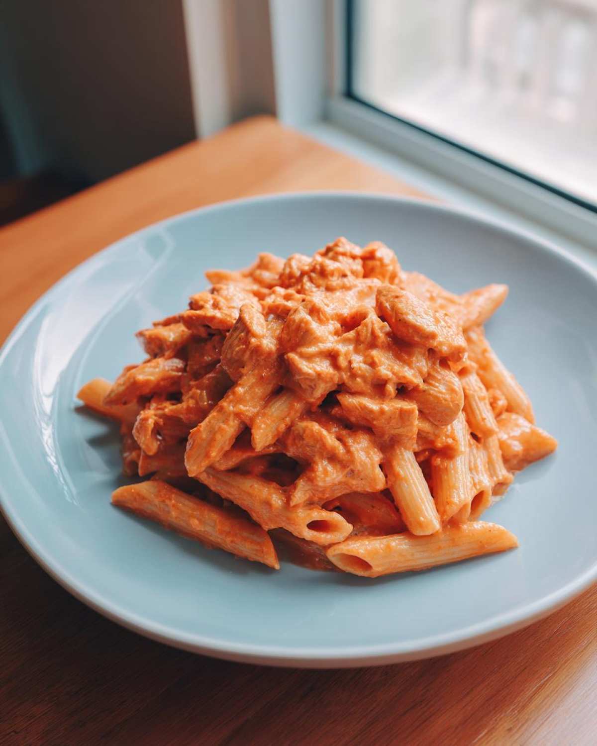 A serving of One Pot Creamy Tomato Pasta with Chicken featuring penne pasta and chunks of chicken in a rich, orange-red sauce.