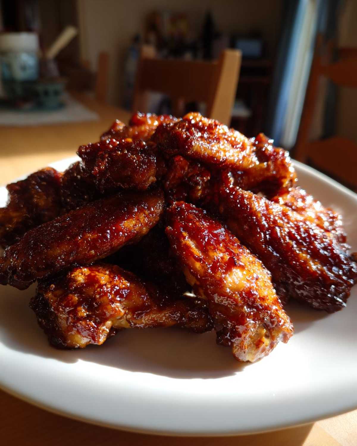 A pile of glossy, dark brown Sticky BBQ Chicken Wings Crispy Oven Style on a white plate.