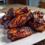 A pile of perfectly cooked Sticky BBQ Chicken Wings with Honey Glaze, featuring a dark, caramelized, and glossy coating.
