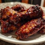 A plate piled high with glossy, dark brown Sticky BBQ Chicken Wings coated in a thick honey glaze.