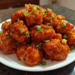 A white plate piled high with glistening Sticky Sweet Chili Chicken Easy Recipe pieces, garnished with green onions.