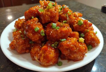 A white plate piled high with glistening Sticky Sweet Chili Chicken Easy Recipe pieces, garnished with green onions.