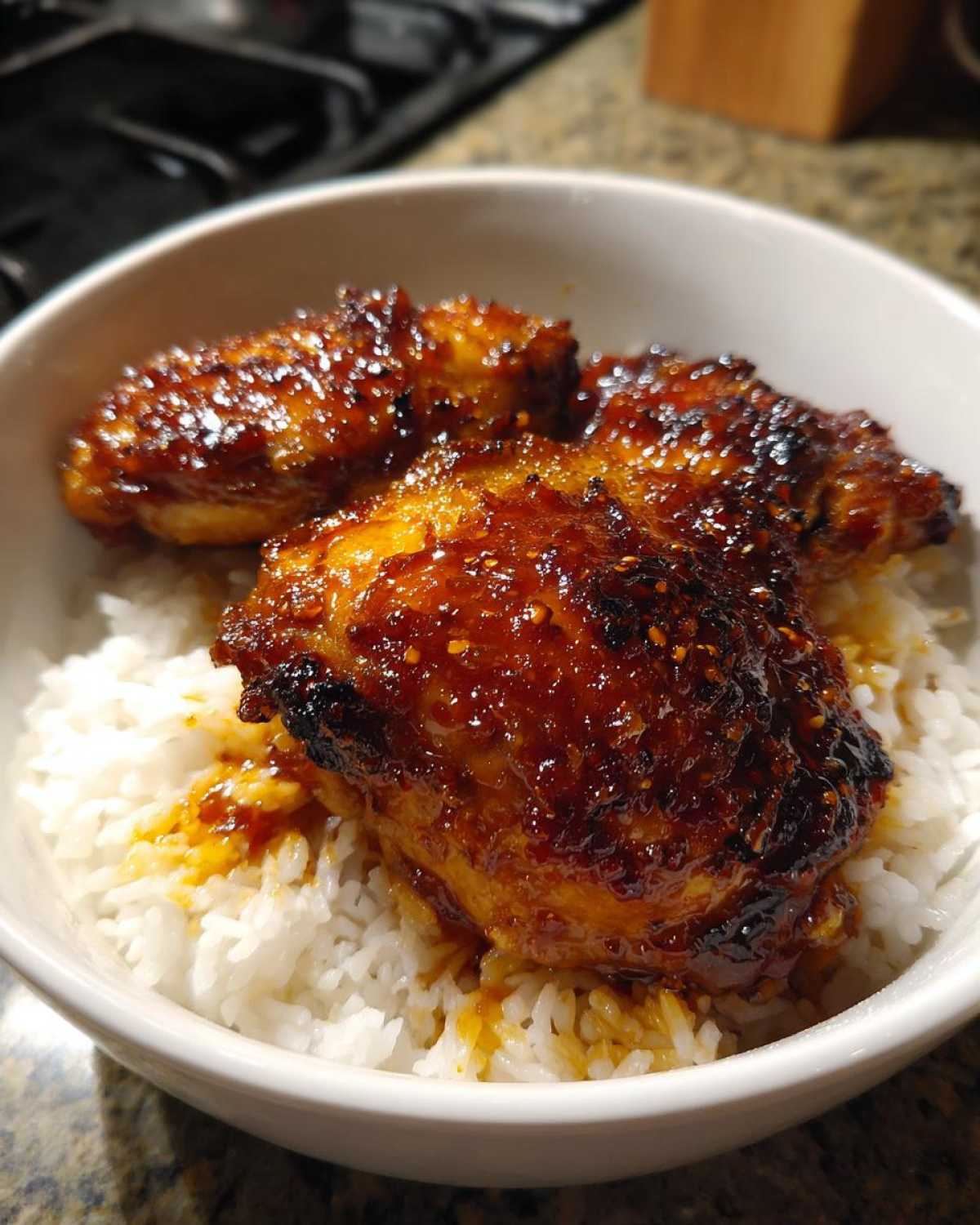 Three glazed Sticky Sweet Chili Chicken Thighs resting on a bed of white rice in a white bowl.