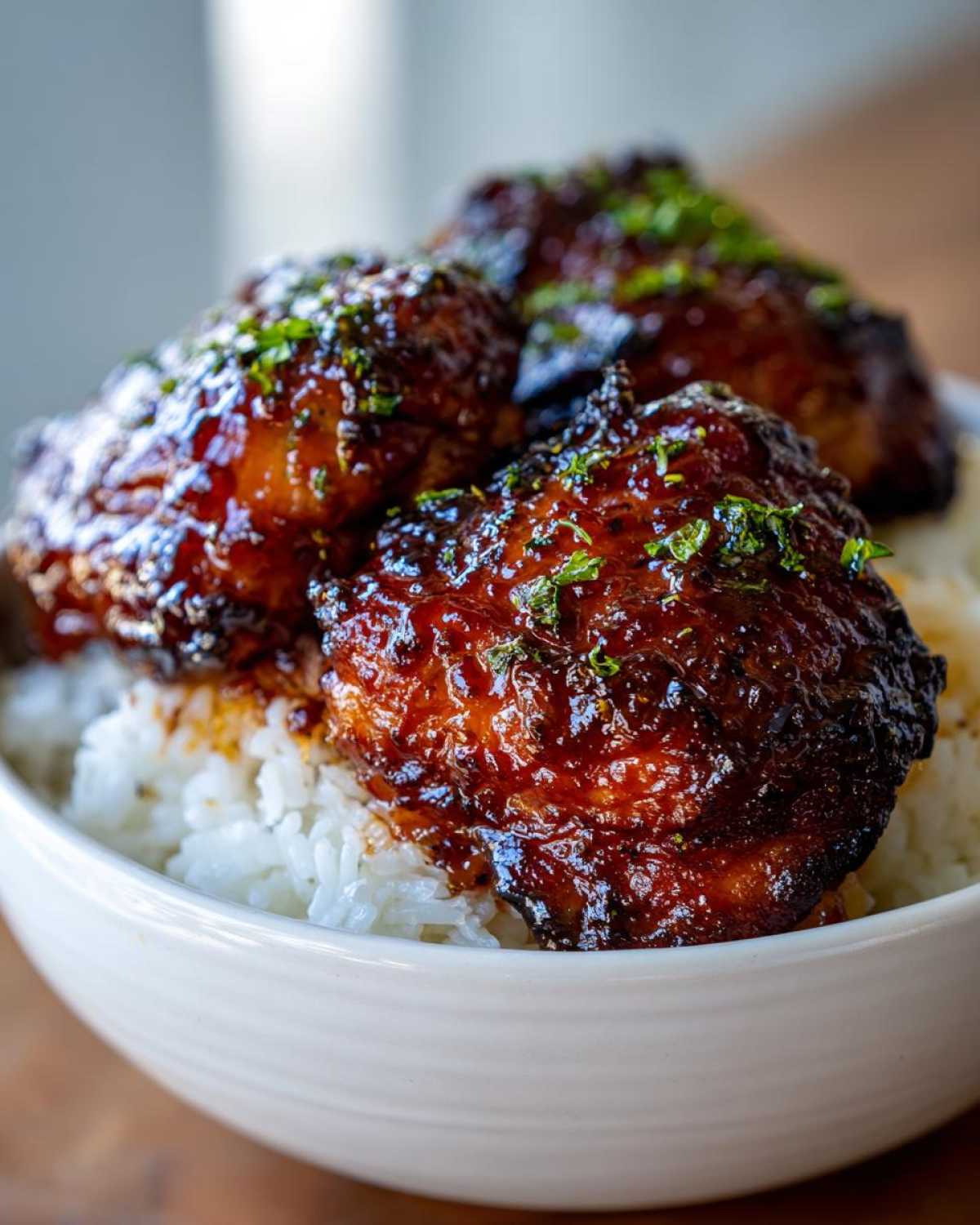 Three glazed Sticky Sweet Chili Chicken Thighs served over a bed of white rice in a white bowl.