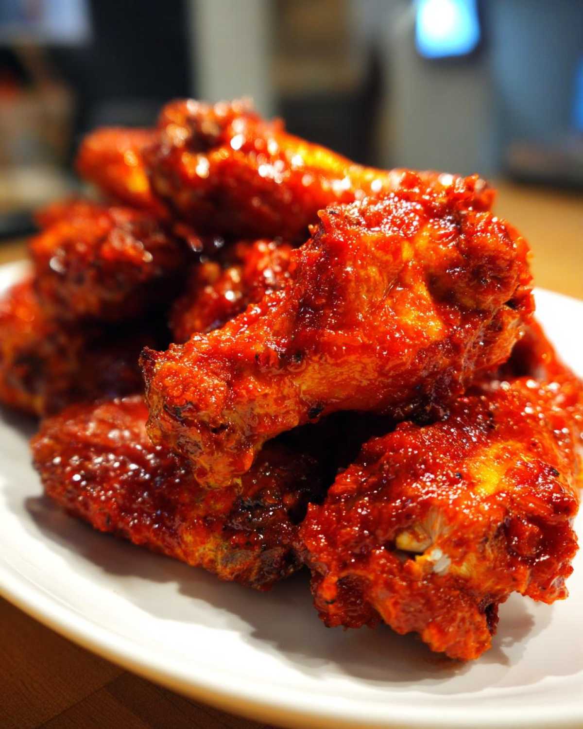 A close-up of several glistening, bright red Sticky Sweet Chili Chicken Wings Oven Baked piled on a white plate.