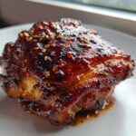 Close-up of a single, perfectly glazed Sticky Teriyaki Chicken Thighs with Garlic, topped with sesame seeds.