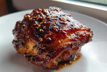 Close-up of a single, perfectly glazed Sticky Teriyaki Chicken Thighs with Garlic, topped with sesame seeds.