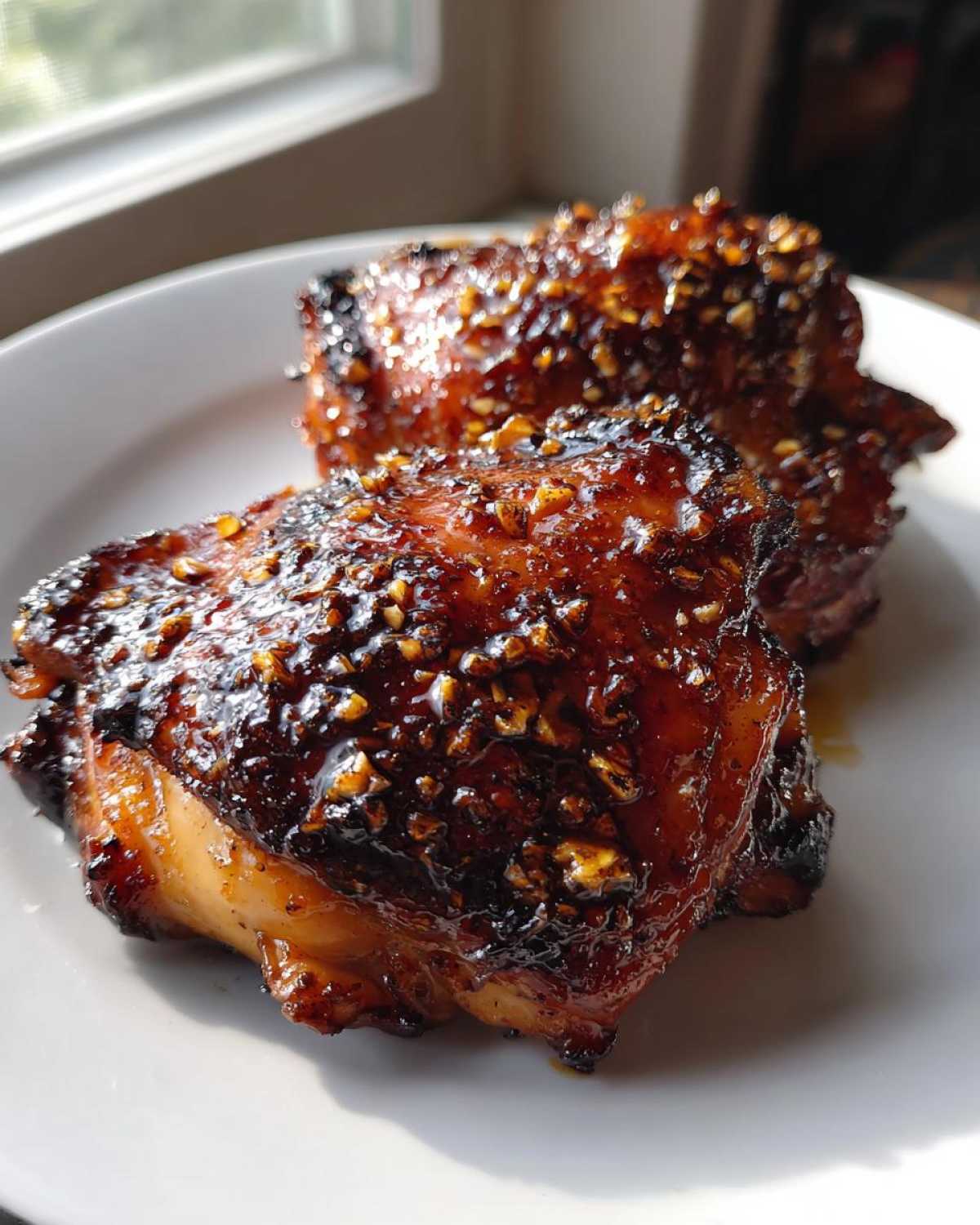 Two pieces of Sticky Teriyaki Chicken Thighs with Garlic, glistening with a dark, caramelized glaze and topped with minced garlic.