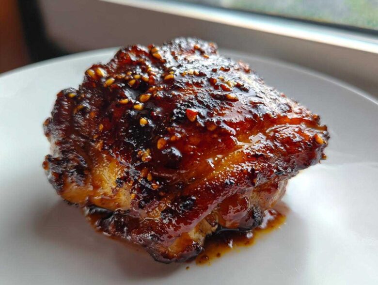 Close-up of a single, perfectly glazed Sticky Teriyaki Chicken Thighs with Garlic, topped with sesame seeds.