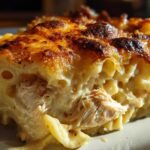 A close-up cross-section of Cheesy Baked Chicken Alfredo showing creamy pasta, shredded chicken, and a deeply browned, crispy cheese top.