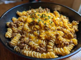 Close-up of Cheesy Ground Beef Pasta Skillet with melted cheddar cheese and parsley garnish in a dark skillet.