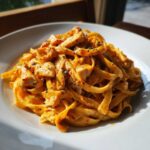 A close-up of rich, orange-hued Creamy Cajun Chicken Pasta with fettuccine noodles and diced chicken, seasoned with dark herbs.