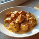 Close-up of cubed chicken pieces coated in a rich, orange-hued Creamy Cajun Chicken Skillet sauce.