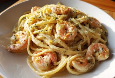 A close-up of a serving of Creamy Lemon Shrimp Pasta with Garlic Sauce, topped with lemon zest and herbs.