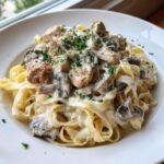 A close-up of fettuccine pasta topped with chicken, mushrooms, and rich, creamy mushroom chicken pasta with garlic sauce, garnished with parsley.