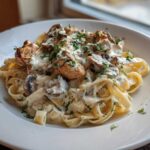 A plate of fettuccine pasta tossed in a rich, creamy mushroom chicken pasta with garlic sauce, garnished with parsley.