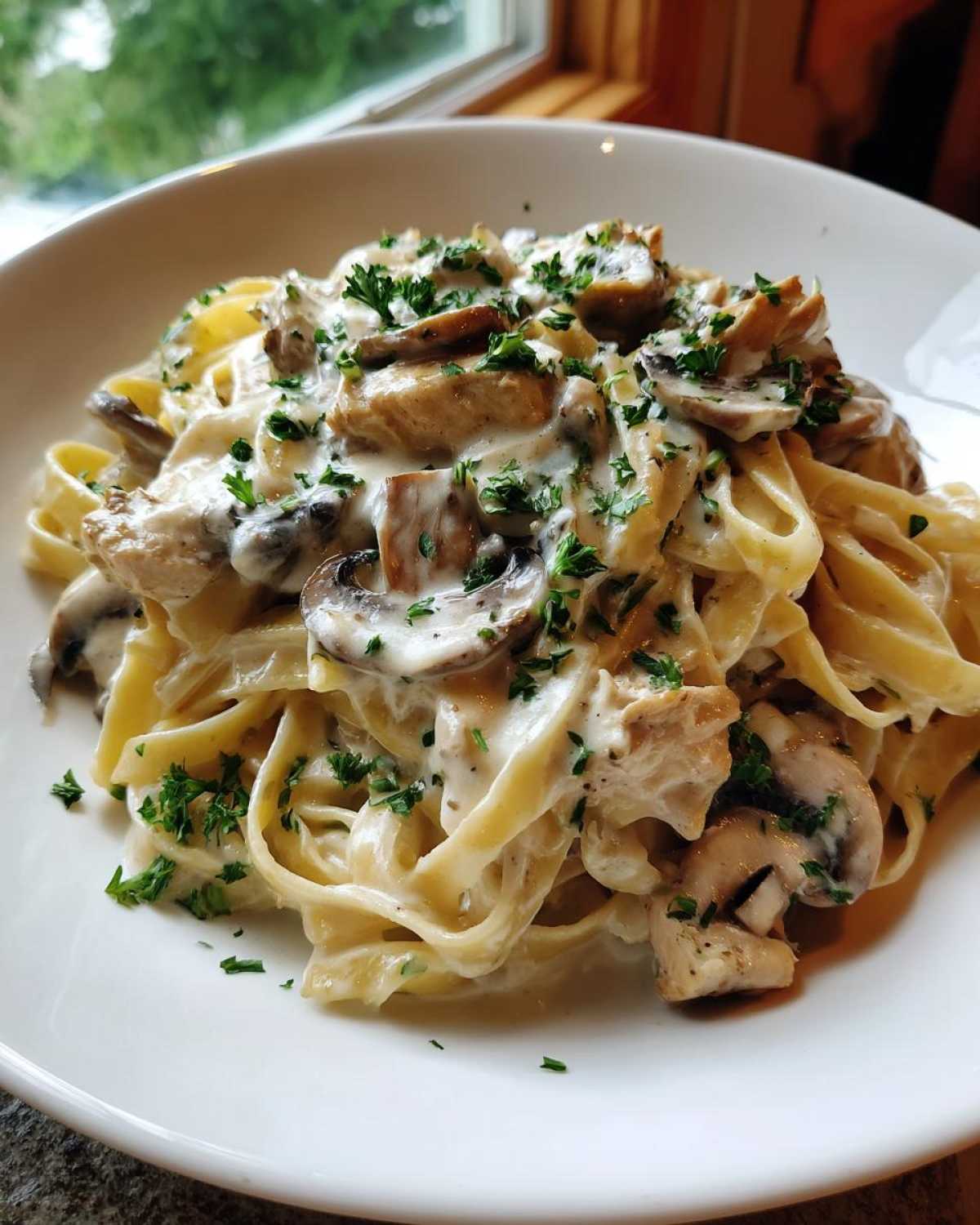 A close-up of a white bowl filled with Creamy Mushroom Chicken Pasta with Garlic Sauce, garnished with parsley.