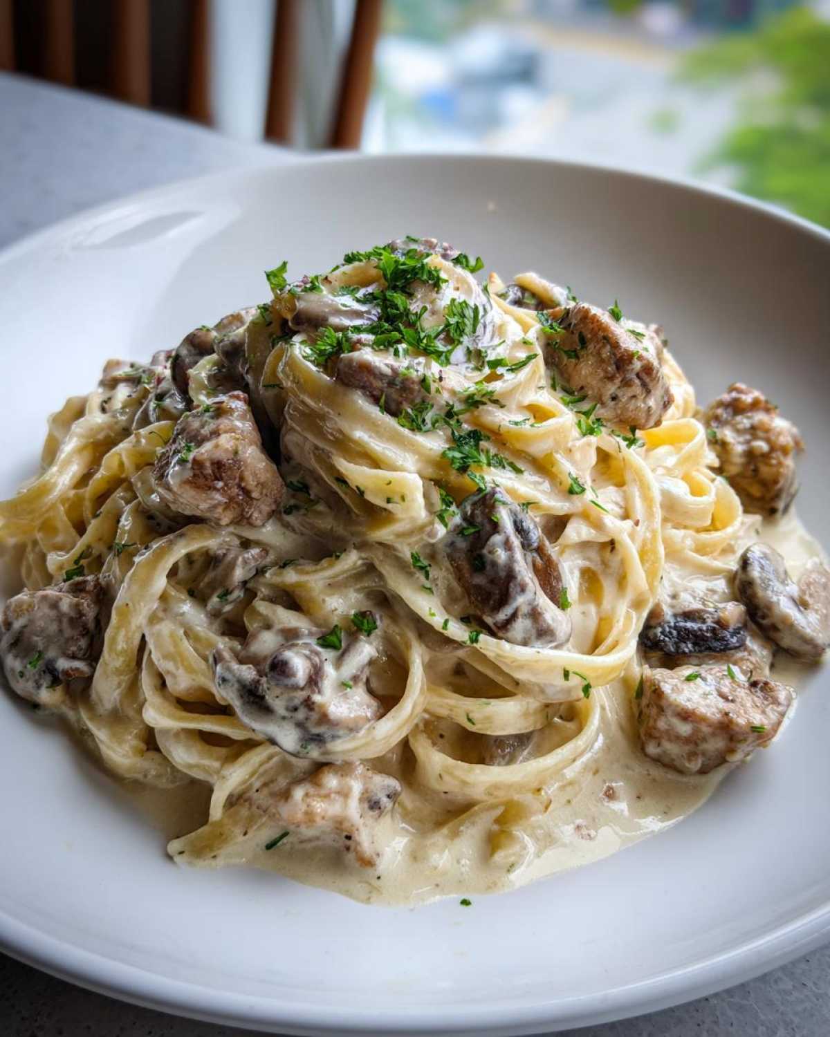 Close-up of fettuccine pasta tossed in a rich, creamy mushroom chicken pasta sauce, garnished with parsley.