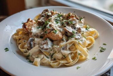 A plate of fettuccine pasta tossed in a rich, creamy mushroom chicken pasta with garlic sauce, garnished with parsley.