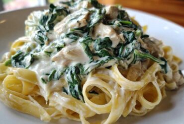 Close-up of fettuccine pasta topped with rich Alfredo sauce, chicken pieces, and wilted spinach in Creamy Spinach Chicken Pasta.