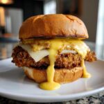A juicy Crispy Chicken Burger topped with melted cheese and dripping honey mustard sauce on a brioche bun.