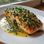 Close-up of a perfectly cooked fillet of Garlic Butter Salmon with Lemon Garlic Sauce, topped with fresh herbs.
