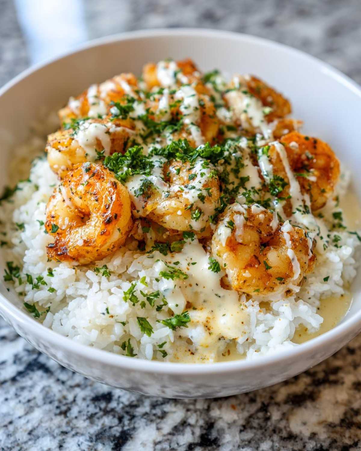 Close-up of a Garlic Butter Shrimp Rice Bowl topped with creamy garlic sauce and fresh parsley.