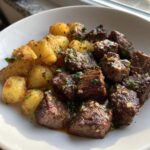 A white bowl filled with juicy Garlic Butter Steak Bites next to golden crispy potatoes, garnished with parsley.