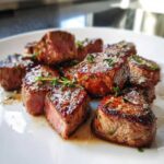Close-up of seared Garlic Butter Steak Bites with a juicy pink center, garnished with thyme.