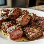 Close-up of perfectly seared Garlic Butter Steak Bites with a juicy pink center, glistening in butter sauce and herbs.