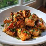 Close-up of glossy, bite-sized Honey Butter Garlic Salmon Bites garnished with fresh parsley.