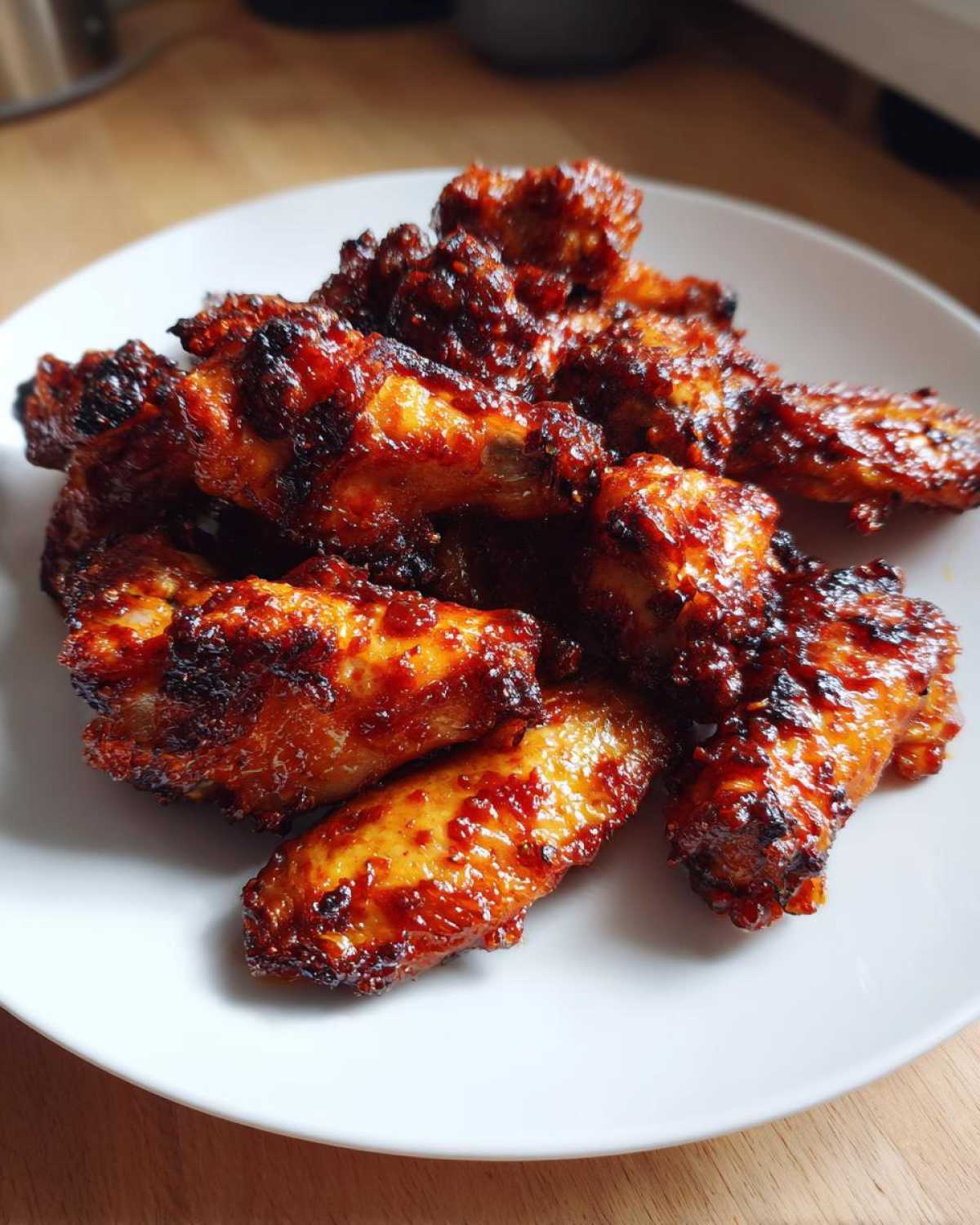 A pile of glossy, caramelized Honey Sriracha Chicken Wings Crispy Oven Baked served on a white plate.