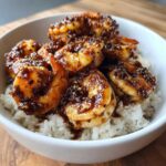 Close-up of Spicy Honey Garlic Shrimp glazed in a dark sauce, served over fluffy white rice in a white bowl.