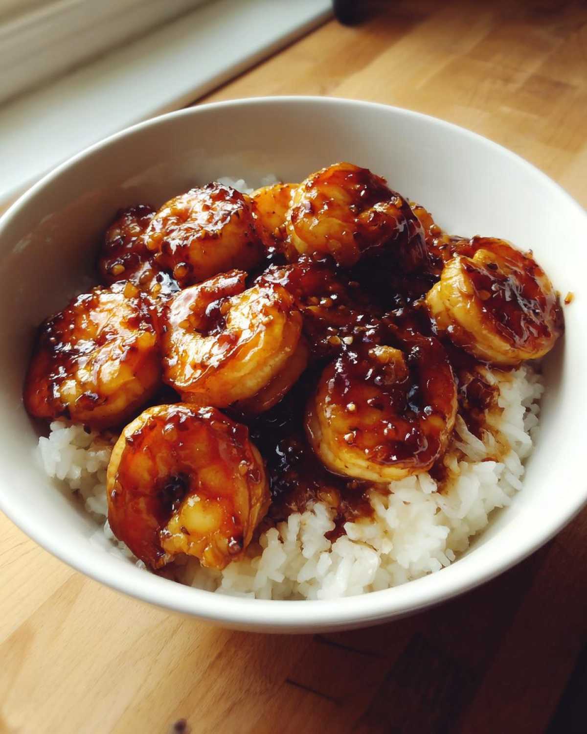 Close-up of Spicy Honey Garlic Shrimp generously coated in sauce served over white rice in a white bowl.