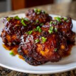 Close-up of four Sticky Honey Soy Chicken Thighs with Garlic, coated in a dark, glossy glaze and topped with chopped green onions.