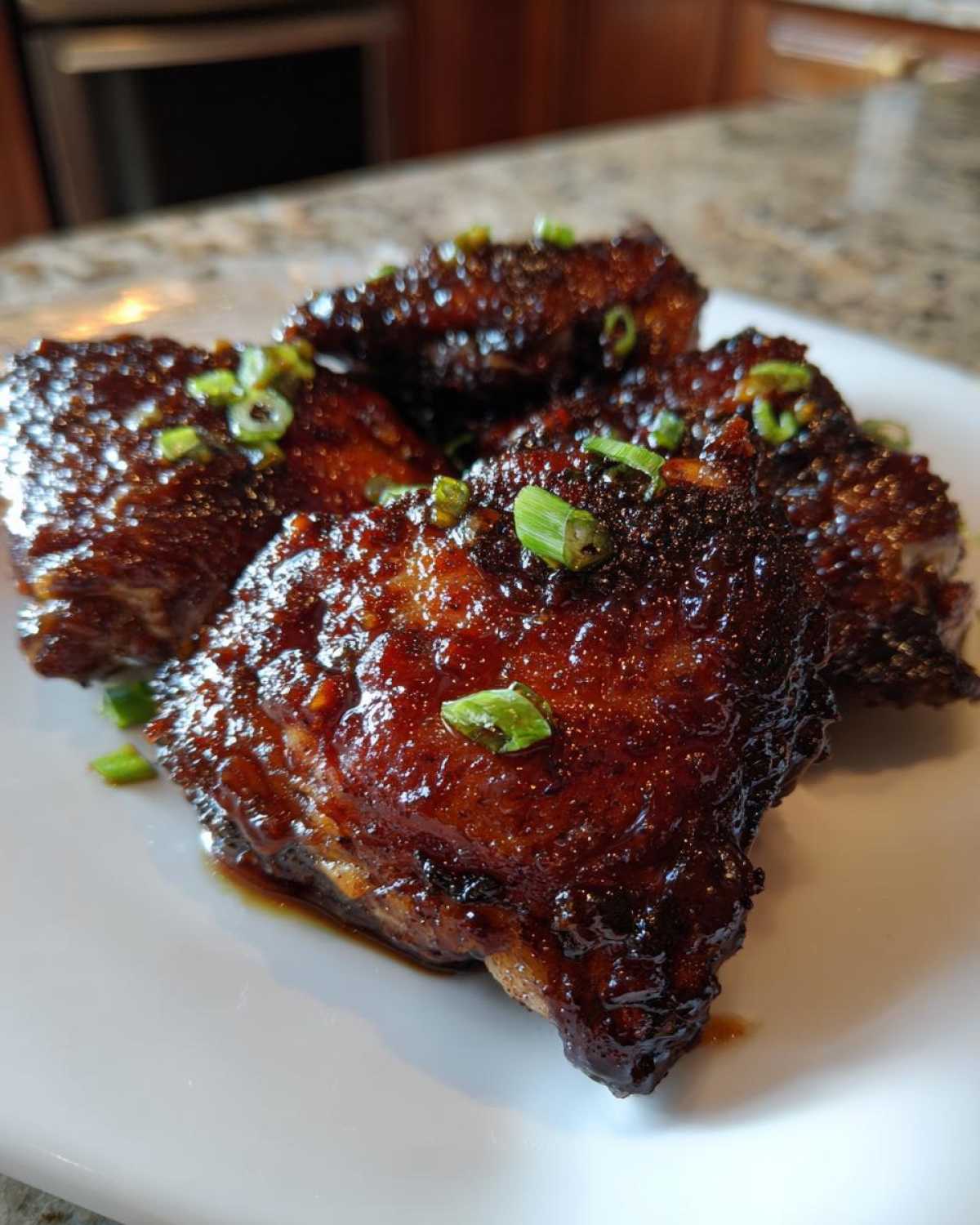 Close-up of Sticky Honey Soy Chicken Thighs with Garlic, coated in a dark, glossy glaze and topped with sliced green onions.