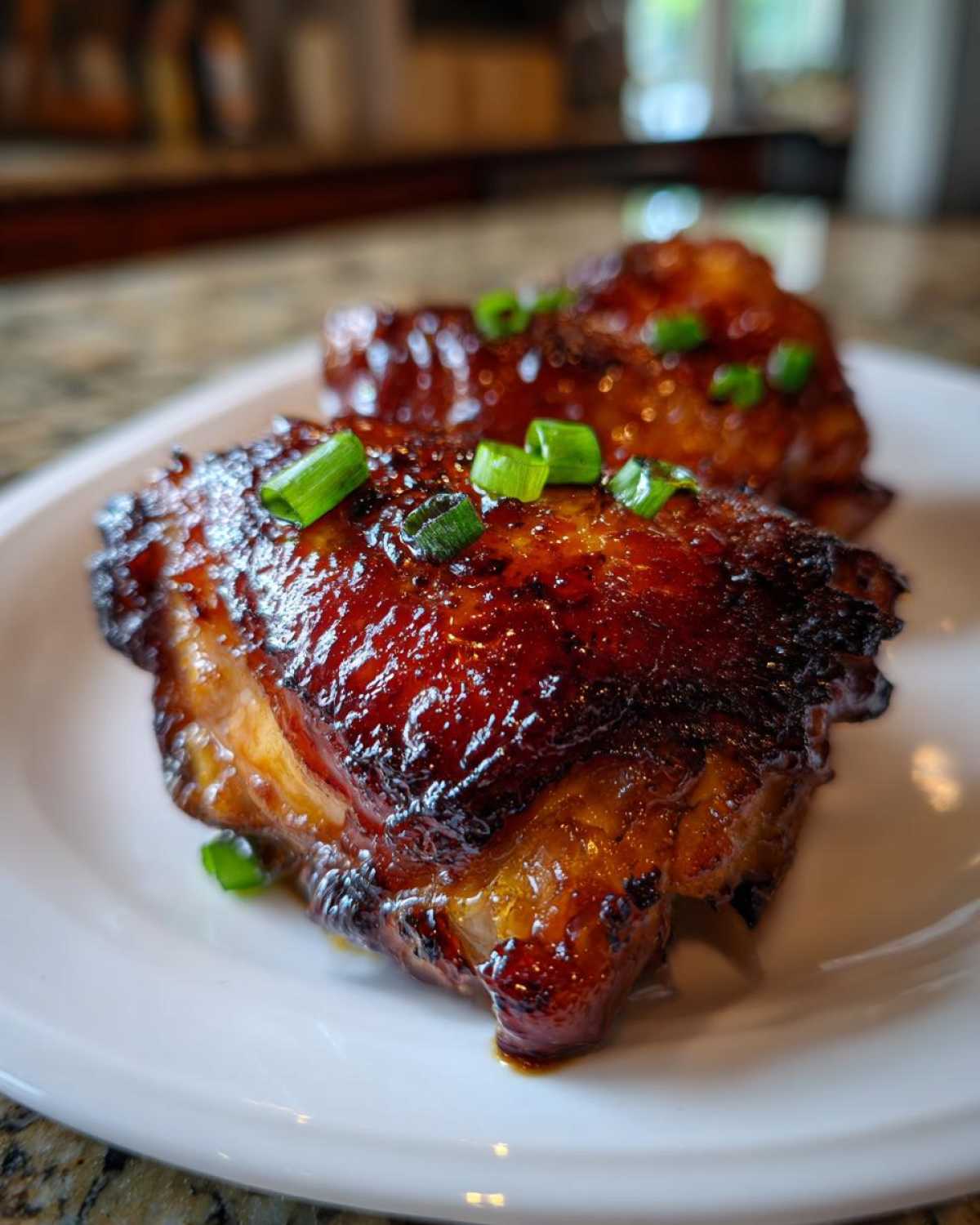 Close-up of two perfectly glazed Sticky Honey Soy Chicken Thighs with Garlic, garnished with fresh green onions.