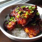 Close-up of Sticky Sweet Chili Chicken Skillet pieces glazed in sauce and topped with green onions, served over white rice in a bowl.