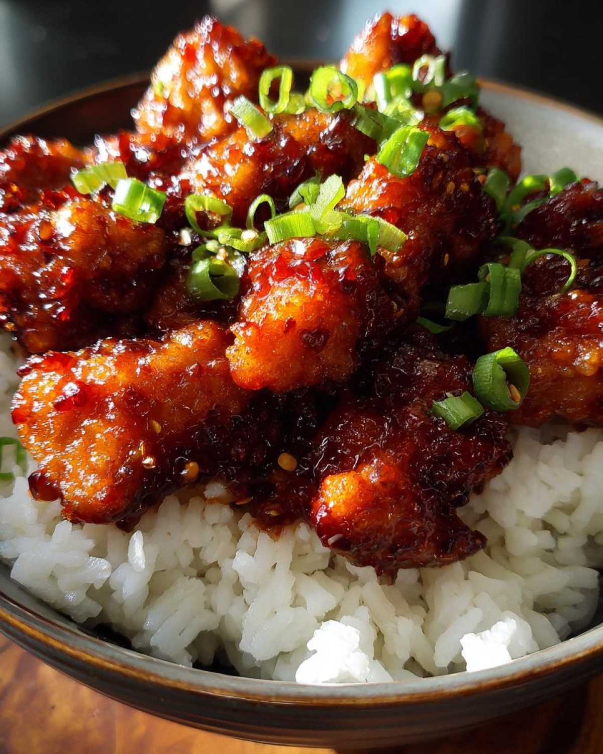 Close-up of crispy chicken pieces coated in a dark, glossy sauce, served over white rice and garnished with green onions, featuring the Sticky Sweet Chili Chicken Skillet.