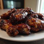 A pile of glossy, dark glazed chicken wings, representing the Sticky Teriyaki Chicken Easy Weeknight Meal, served on a white plate.