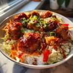 A close-up of a Sweet Chili Chicken Bowl with rice, shredded cabbage, carrots, and topped with sesame seeds.
